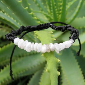 May include: A white moonstone bracelet with black cord. The bracelet is tied with a knot and has a simple design.