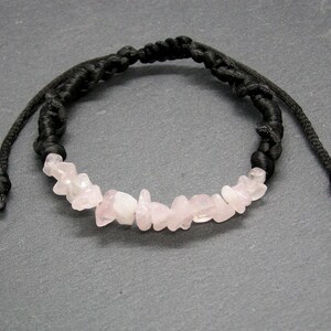 Puede incluir: Un brazalete de cordón negro con chips de cuarzo rosa. El brazalete es ajustable con un nudo deslizante.