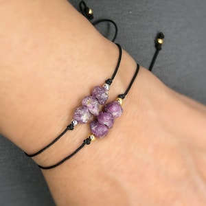 Peut inclure: Un bracelet simple avec un charme en pierre précieuse violette et un cordon noir. Le bracelet est réglable avec un nœud coulissant.