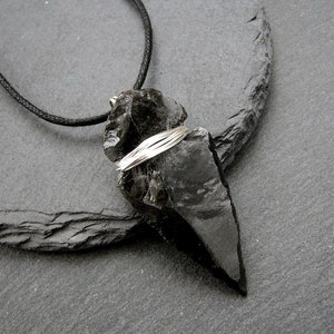 Può includere: Un ciondolo in ossidiana nera con un avvolgimento di filo d'argento, appeso a un cordoncino nero.