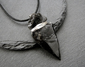 Puede incluir: Un colgante de obsidiana negra con un envoltorio de alambre plateado, colgado de un cordón negro.