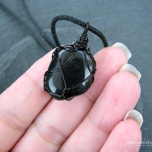 May include: Black gemstone pendant wrapped in black wire, hanging from a black cord.
