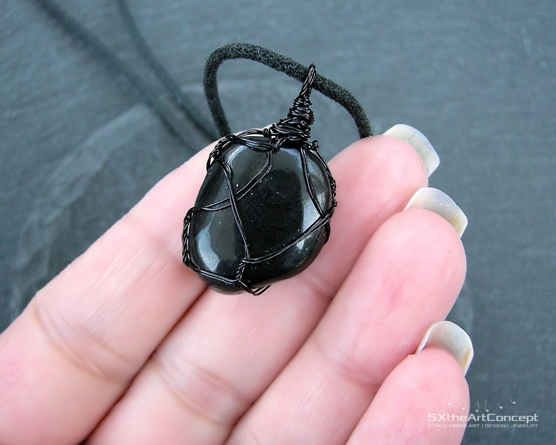 May include: Black gemstone pendant wrapped in black wire, hanging from a black cord.