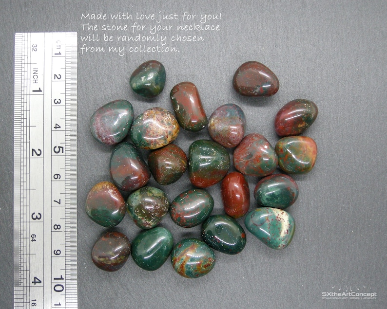 Op de afbeelding: Een verzameling gepolijste edelstenen in groen, rood en bruin. De stenen zijn glad en afgerond, met een liniaal die centimeters aangeeft. Tekst: "Made with love just for you! The stone for your necklace will be randomly chosen from my collection."