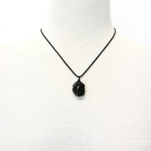 May include: A black gemstone pendant necklace with a black cord. The pendant is a rough, natural-looking stone.