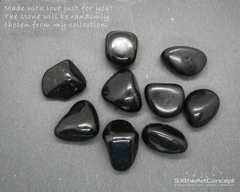 May include: A collection of nine smooth, black stones. The stones are tumbled and polished, and they have a glossy finish. The stones are arranged on a gray surface. The text "Made with love just for you! The stone will be randomly chosen from my collection." is written above the stones. The text "SXtheArtConcept STALO XINAFRI ART DESIGN JEWELRY" is written below the stones.