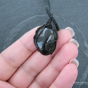 May include: A black stone pendant wrapped in black wire, hanging from a black cord.