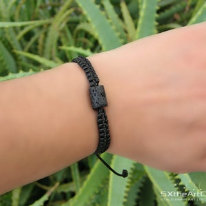 Pode incluir: Um bracelete tran&ccedil;ado preto com uma conta de lava preta. O bracelete &eacute; ajust&aacute;vel e tem um design simples.
