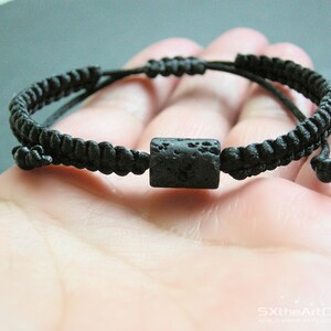 Pode incluir: Um bracelete tran&ccedil;ado preto com uma conta de rocha de lava preta.
