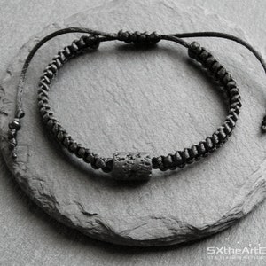 Pode incluir: Um bracelete preto com uma conta de lava preta. O bracelete &eacute; feito de um cord&atilde;o tran&ccedil;ado e tem um design simples.