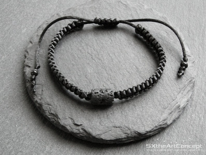 Pode incluir: Um bracelete preto com uma conta de lava preta. O bracelete &eacute; feito de um cord&atilde;o tran&ccedil;ado e tem um design simples.