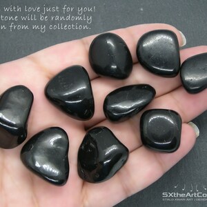 May include: A collection of ten black tumbled stones, likely obsidian, in various shapes and sizes, held in a hand. The stones are smooth and shiny.