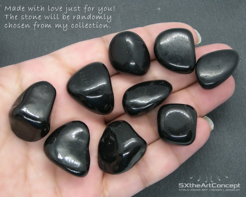 May include: A collection of ten black tumbled stones, likely obsidian, in various shapes and sizes, held in a hand. The stones are smooth and shiny.