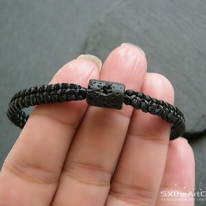 Pode incluir: Um bracelete tran&ccedil;ado preto com uma conta de lava preta.