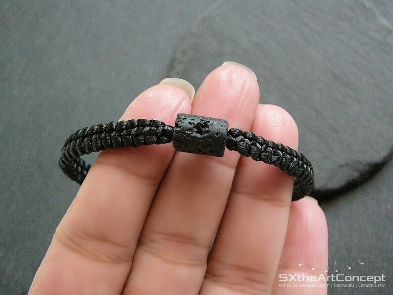 Pode incluir: Um bracelete tran&ccedil;ado preto com uma conta de lava preta.