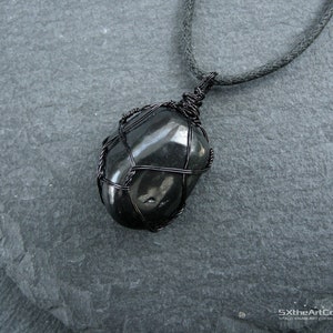 May include: Black gemstone pendant necklace with a wire wrapped design. The pendant is a smooth, black stone with a dark gray background.