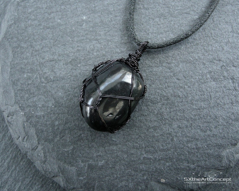 May include: Black gemstone pendant necklace with a wire wrapped design. The pendant is a smooth, black stone with a dark gray background.