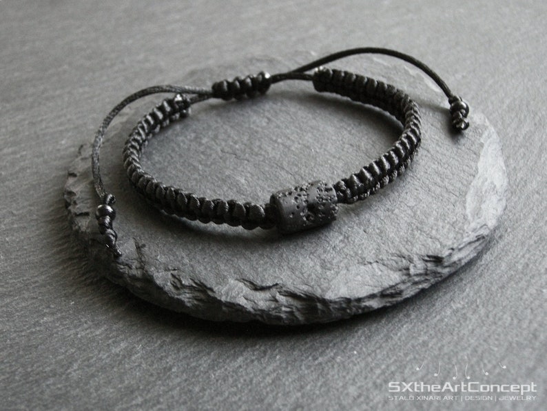 Pode incluir: Um bracelete preto com uma conta de lava preta. O bracelete &eacute; feito de um cord&atilde;o tran&ccedil;ado e tem um design simples.