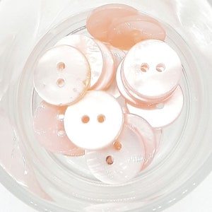 Op de afbeelding: Een kom met roze, ronde knopen met twee gaten. De knopen zijn gemaakt van parelmoer.