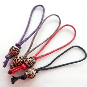 以下が含まれることがあります： 装飾的な金属ビーズが付いた、4色の異なるコード。コードは紫、茶色、赤、黒です。