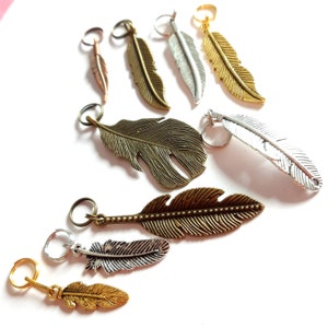 Könnte beinhalten: Sortiment an Federschmuck in Gold-, Silber- und Bronzetönen. Die Charms sind in verschiedenen Größen und Formen, einige mit filigranen Details. Diese Charms sind perfekt, um Schmuck, Kunsthandwerk und anderen Projekten einen Hauch von Verspieltheit und Eleganz zu verleihen.