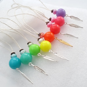 以下が含まれることがあります： 銀と金の羽根チャームが付いた、カラフルなビーズネックレスのセットです。各ネックレスには、パープル、ピンク、オレンジ、イエロー、グリーン、ブルー、ターコイズなど、異なる色の大きな丸いビーズが付いています。