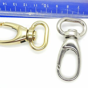 May include: Two metal swivel clasps, one gold and one silver. The clasps are both open and ready to be attached to a strap or chain.