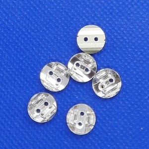 Peut inclure: Six boutons argentés avec deux trous chacun. Les boutons ont un design texturé légèrement en relief.