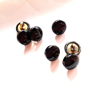 Op de afbeelding: Zes zwarte ronde knopen met een gouden steel. De knopen zijn glanzend en hebben een glad oppervlak.