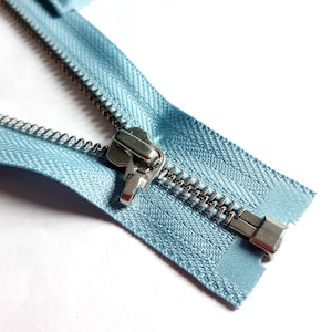 May include: A close-up of a light blue zipper with a silver zipper pull. The zipper is open and the teeth are visible.
