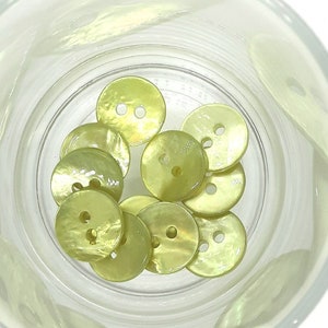 Könnte beinhalten: Eine Sammlung von 10 hellgelben Knöpfen mit jeweils zwei Löchern. Die Knöpfe befinden sich in einem durchsichtigen Glasgefäß.