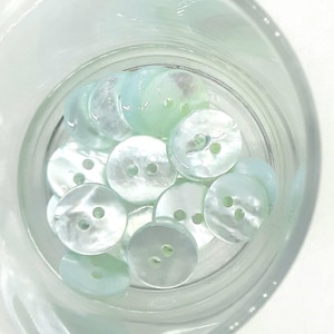 Könnte beinhalten: Eine Sammlung von hellblauen und weißen irisierenden Knöpfen in einem Glasgefäß. Die Knöpfe sind rund und haben zwei Löcher.