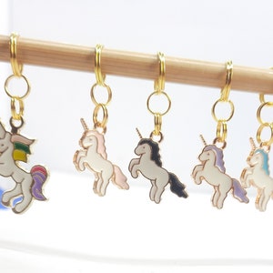 Könnte beinhalten: Eine Sammlung farbenfroher Einhorn-Anhänger mit goldfarbenen Ringen, die an einem Holzstab hängen. Jeder Anhänger hat eine unterschiedlich farbige Mähne und einen Schwanz, darunter Rosa, Lila und Blau. Die Anhänger sind für Bastelarbeiten gedacht.