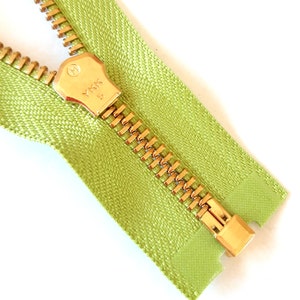 May include: Close-up of a gold zipper with a green tape. The zipper pull has the text "YKK" on it.