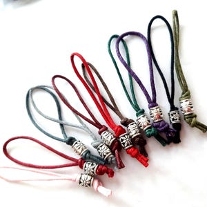 Könnte beinhalten: Sortiment an bunten Schnüren mit silbernen Metallperlen am Ende. Die Schnüre sind in verschiedenen Farben, darunter Rot, Grün, Blau, Lila und Schwarz.