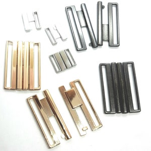 Könnte beinhalten: Sortiment an Metall-BH-Gleitern in Gold-, Silber- und Schwarz-Finish. Die Gleiter sind in verschiedenen Größen und Ausführungen, einschließlich ein- und zweireihiger Designs.