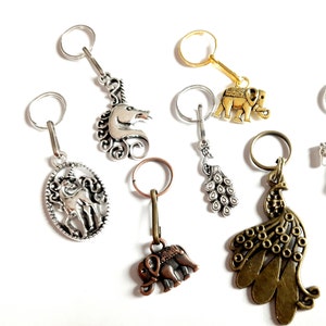 Può includere: Un set di nove portachiavi in argento e oro con ciondoli vari, tra cui un unicorno, un pavone e un elefante. I ciondoli sono dettagliati e intricati.