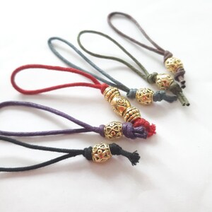 以下が含まれることがあります： 金色の金属ビーズが付いた6本のカラフルなコード。それぞれ異なるデザインです。コードはループ状に結ばれており、ブックマークやジッパーの引き手として使用できます。