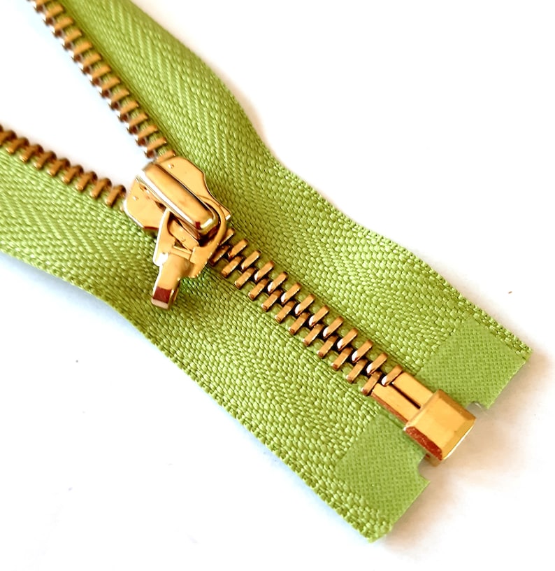 May include: A close-up of a green zipper with a gold metal slider and pull tab.
