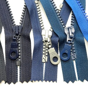 Könnte beinhalten: Verschiedene Reißverschlüsse in verschiedenen Blau- und Grautönen. Die Reißverschlüsse sind geöffnet und zeigen die Zähne und Zipper. Die Zipper sind farblich passend, einige haben silberfarbene Metallzipper.