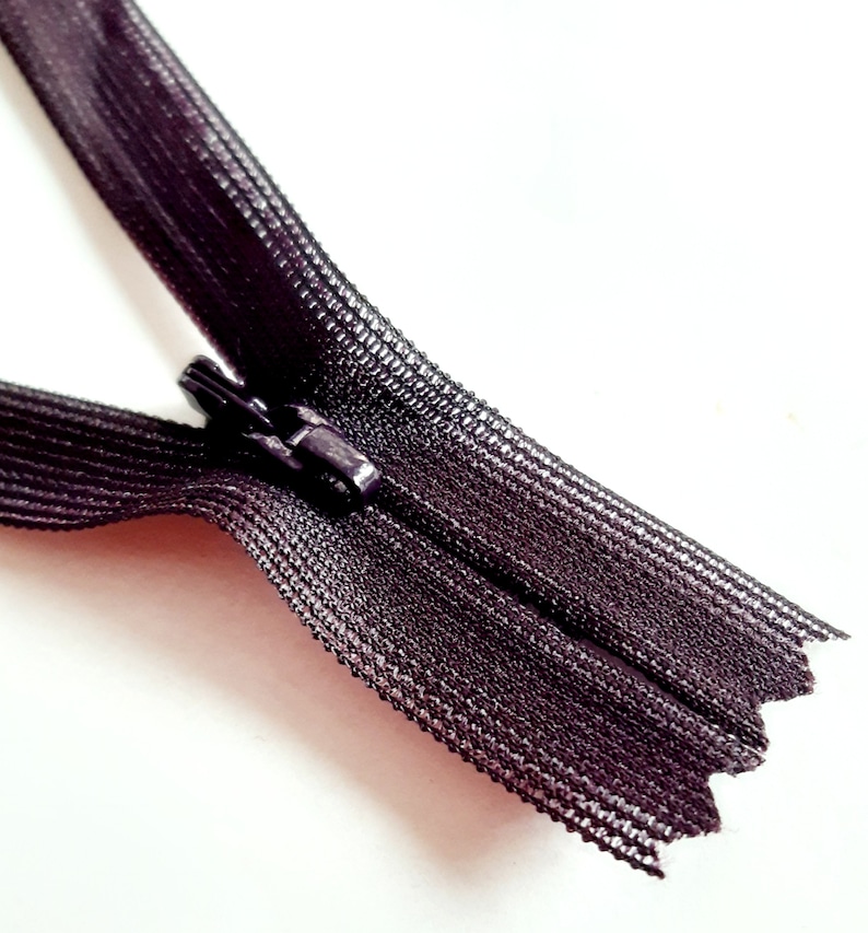 May include: A black zipper with a metal slider. The zipper is closed and the slider is in the centre.