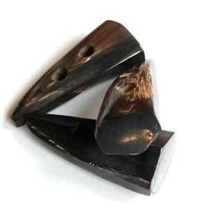 Könnte beinhalten: Drei schwarze Hornknöpfe mit jeweils zwei Löchern. Die Knöpfe sind dreieckig und haben eine glatte, polierte Oberfläche.