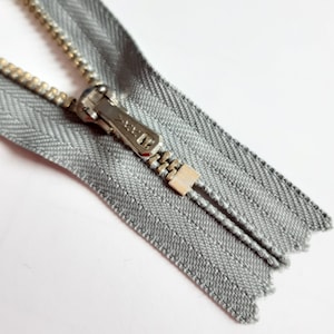May include: A silver zipper with a silver slider and a grey fabric tape. The zipper is open and the slider is in the middle of the tape.