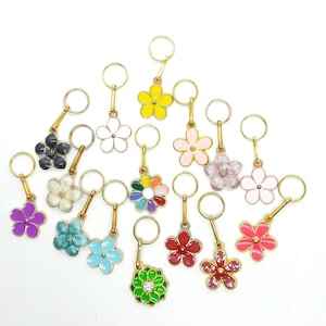 Könnte beinhalten: Sortiment an bunten, blumenförmigen Maschenmarkierern mit goldenen Ringen. Die Markierer sind in verschiedenen Farben, darunter Lila, Blau, Grün, Rot, Rosa, Gelb und Weiß.