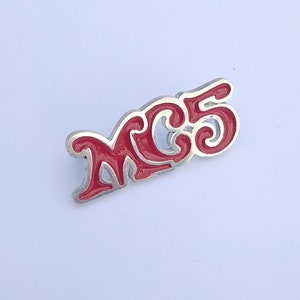 Könnte beinhalten: Ein roter und silberner MC5-Anstecker. Der Anstecker zeigt den Text "MC5" in einer stilisierten Schriftart mit roter Emaille, die die Buchstaben ausfüllt. Der Rand des Ansteckers ist silberfarben. Der Anstecker ist ein Sammlerstück.