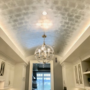 May include: A white kitchen hallway with a vaulted ceiling featuring a silver metallic paint finish. A clear glass chandelier with silver accents hangs from the ceiling. The hallway has white cabinets on both sides and a doorway at the end leading to another room.