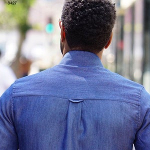 May include: A blue denim shirt with a button-down collar and a yoke detail on the back. The image shows the back of the shirt, with the text "Simplicity Pattern 8427" in the upper left corner.