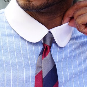 May include: Close-up of a light blue striped shirt with a white collar and a striped tie. The tie features red, gray, and navy blue stripes. The text "Simplicity Pattern 8427" is visible in the upper left corner.