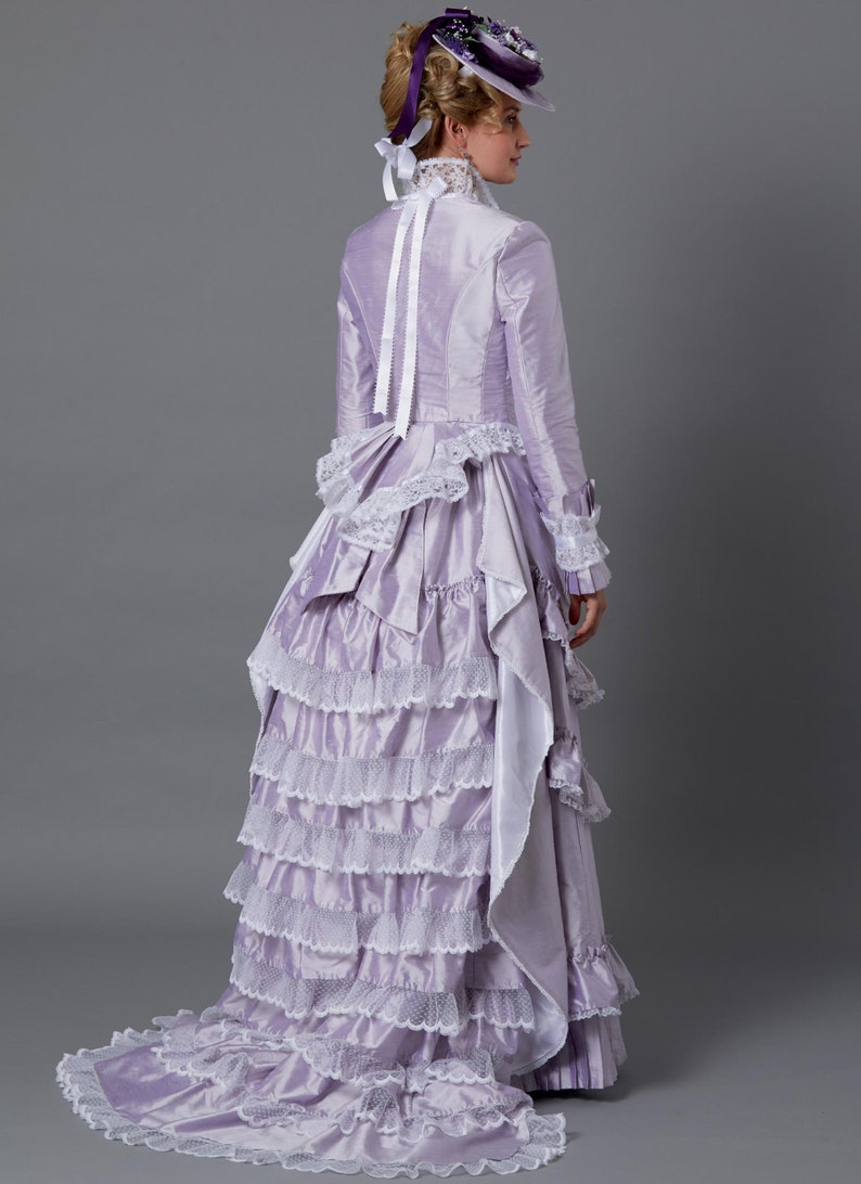 May include: A lavender Victorian-style dress with multiple ruffled layers and white lace trim. The long-sleeved dress features a high collar, a small hat with floral accents, and a long train. The dress is made of a shiny fabric.