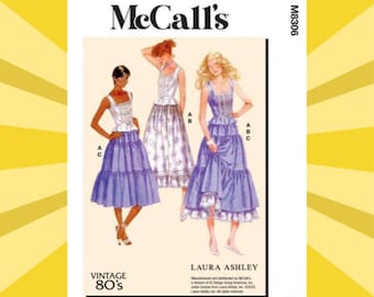 May include: A McCall's M8306 sewing pattern envelope featuring illustrations of three variations of a dress with a fitted bodice and tiered skirt. The text includes McCall's, M8306, Vintage 80's, and Laura Ashley. The illustrations show dresses in white and purple.